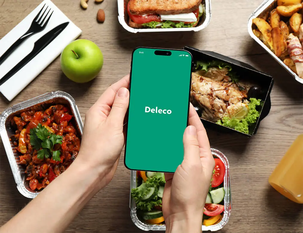 Smartfón zobrazujúci úvodnú obrazovku aplikácie Deleco s pokrmami chutného jedla v pozadí, propagujúci objednávanie zdravých jedál.